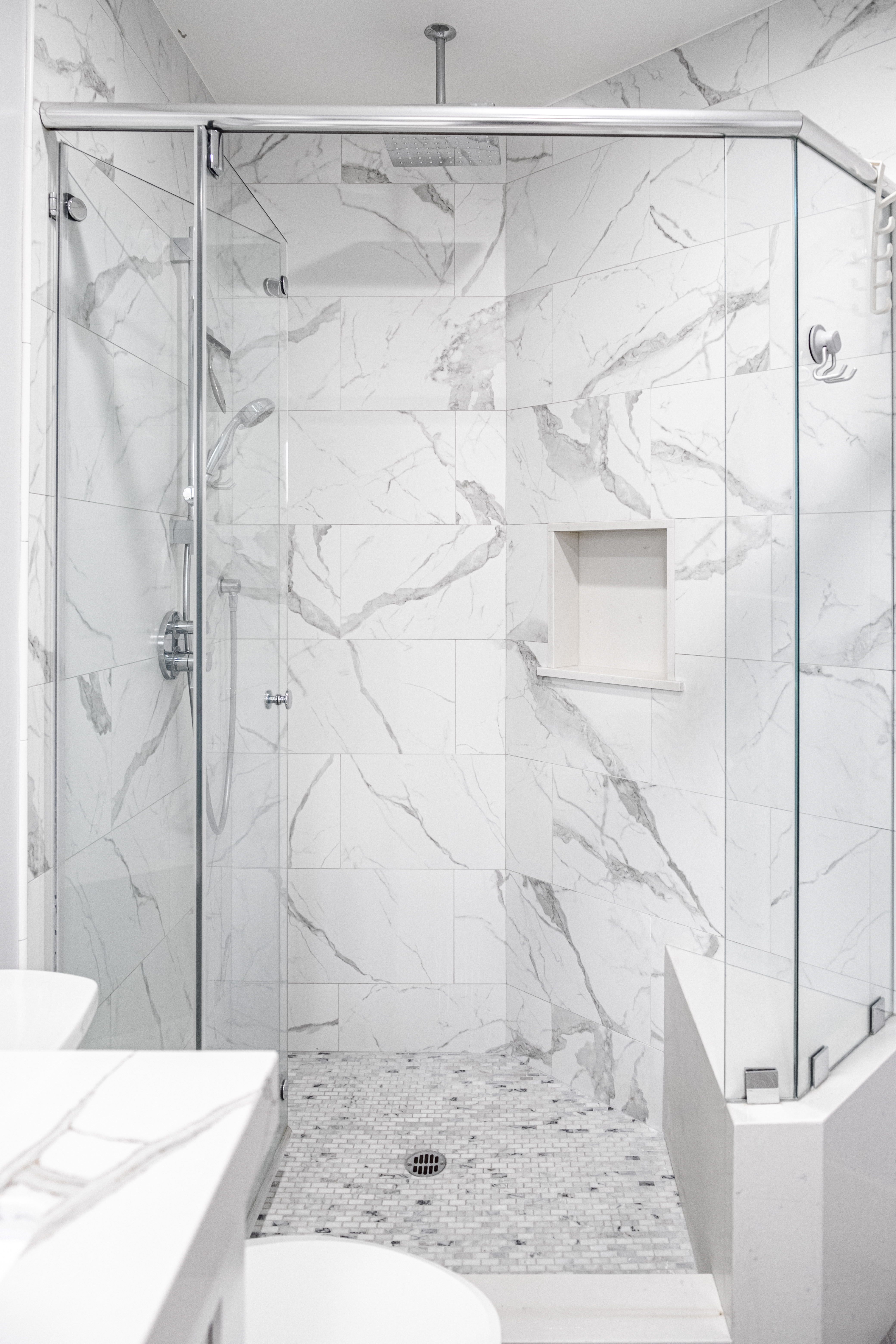 Completed bathroom with marble-look tile shower, glass enclosure, rain head, and mosaic floor