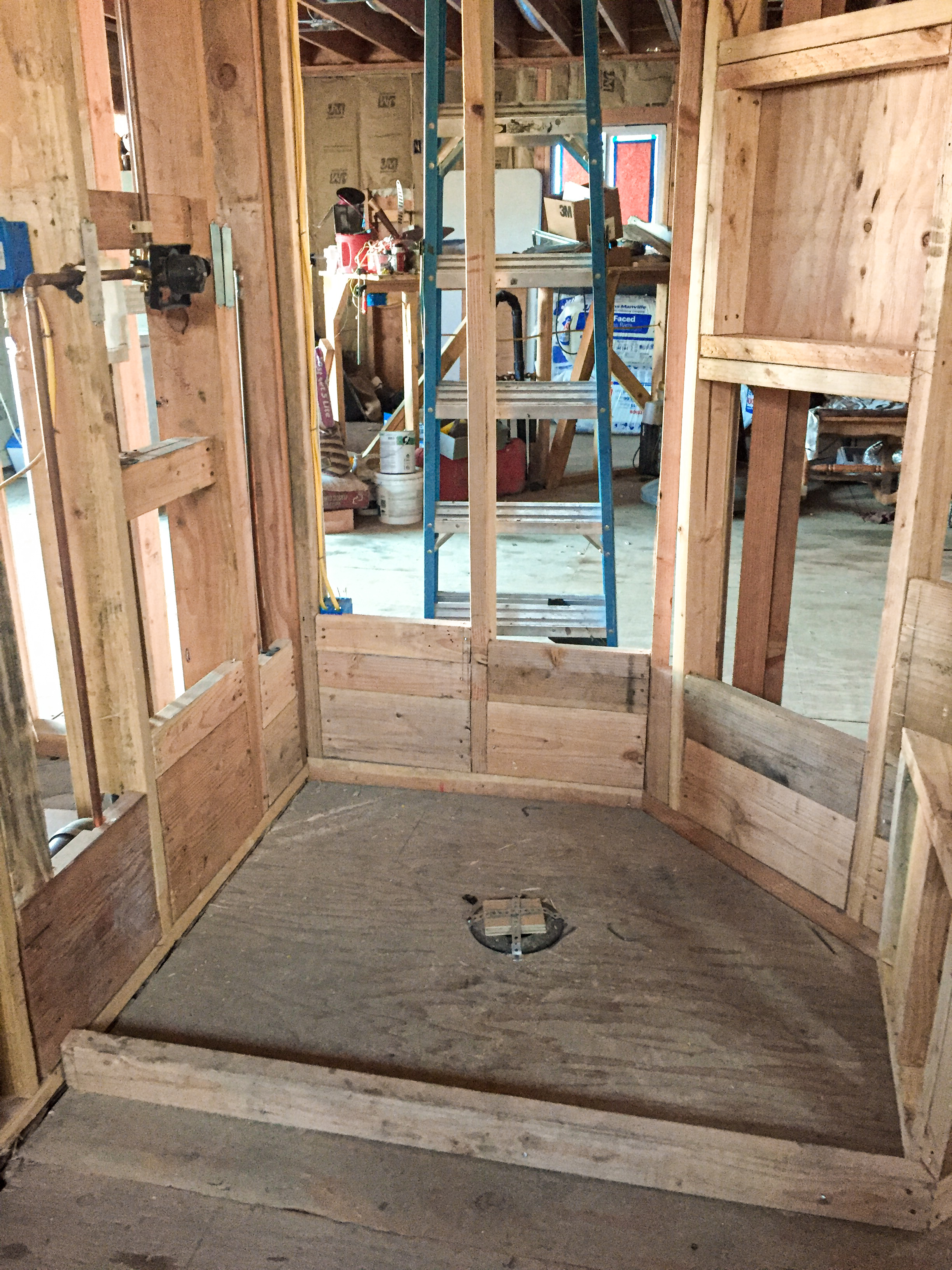 Shower pan framed with raw plywood, plumbing rough-in visible, exposed studs