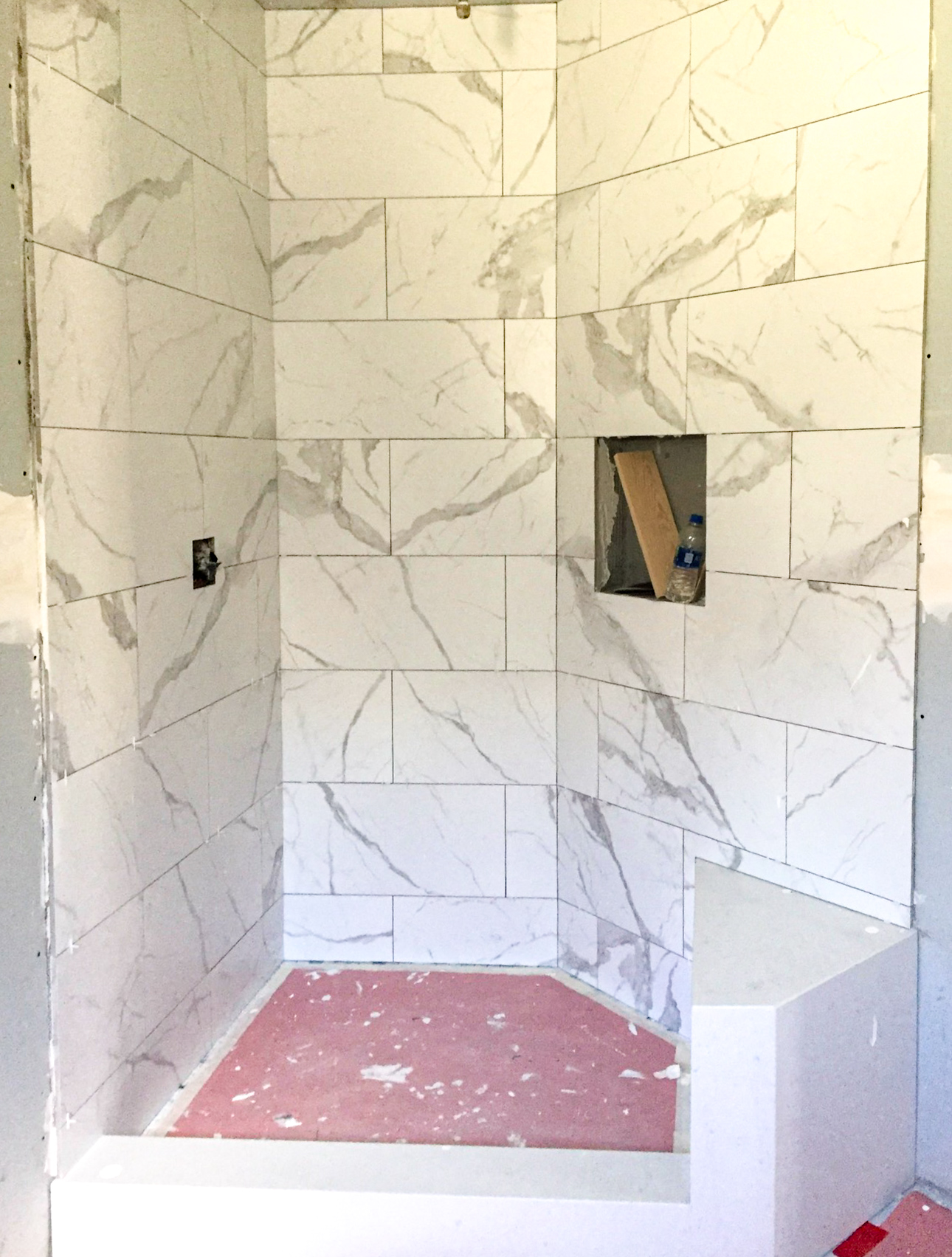 Shower tile installation in progress — marble-look wall tile set, niche roughed in, floor unfinished