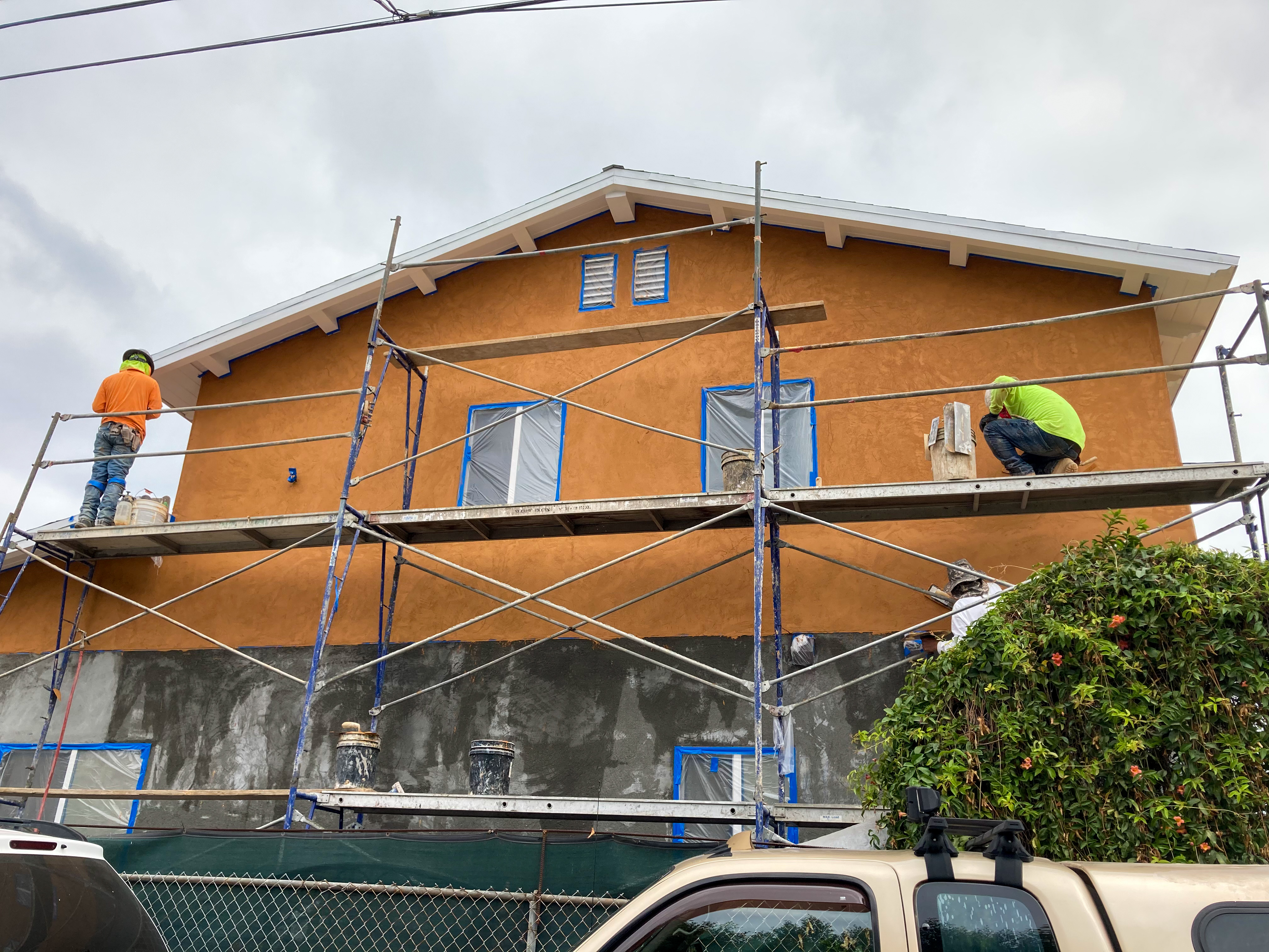 Front elevation with stucco finish coat being applied, crew on scaffolding