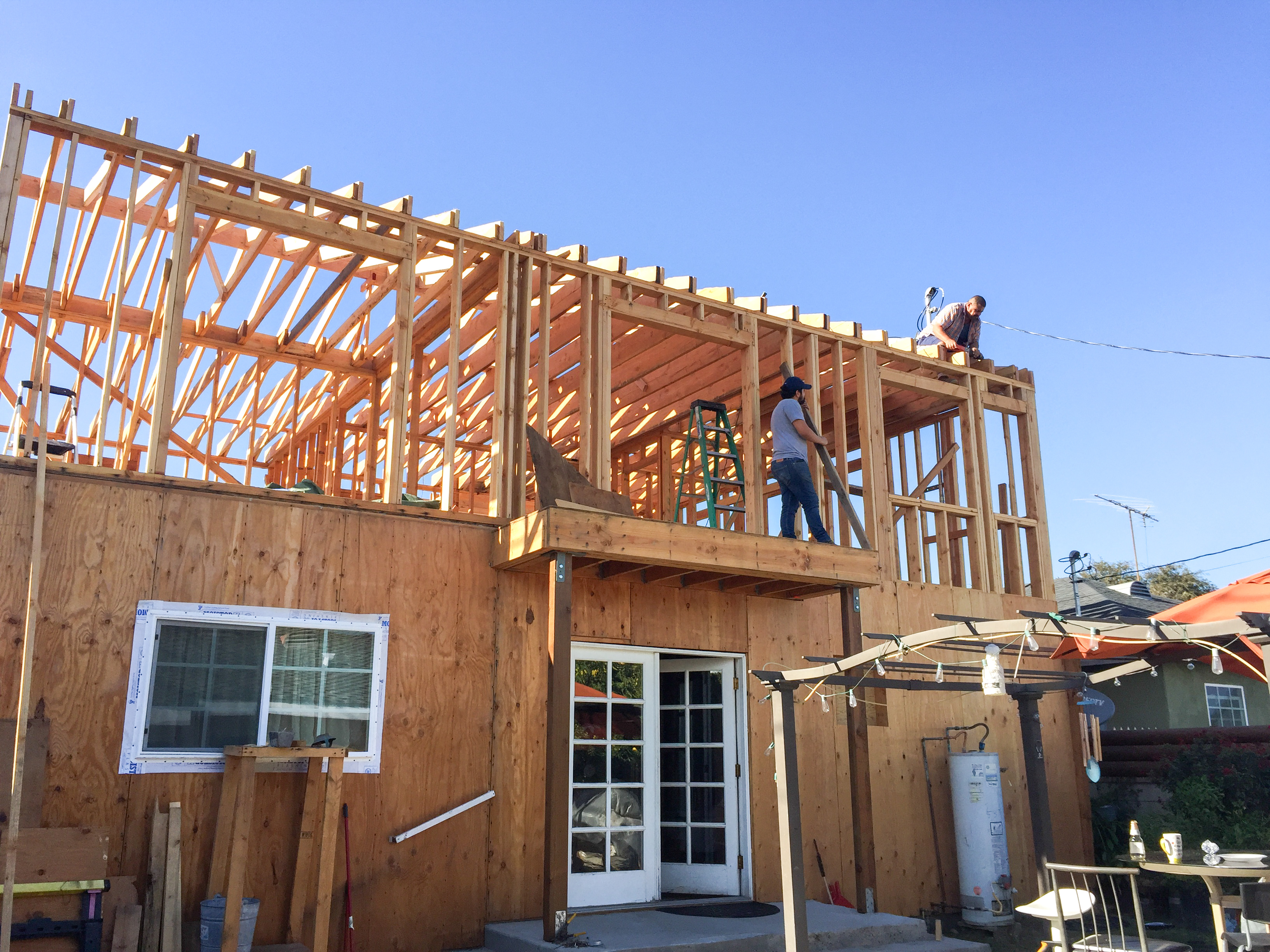 Rear elevation during framing — second-story addition with sheathing, crew on structure